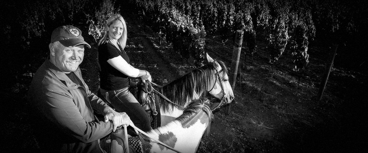 2Hawk Vineyard and Winery Owners Ross and Jen Allen Horseback Riding in Vineyard (Grayscale)